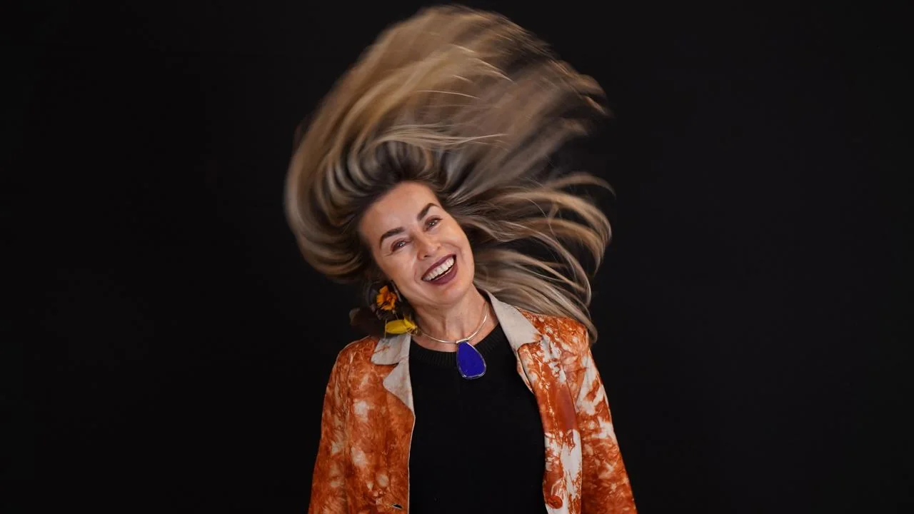 Daniella Prestes em movimento, cabelo no ar, blazer laranja