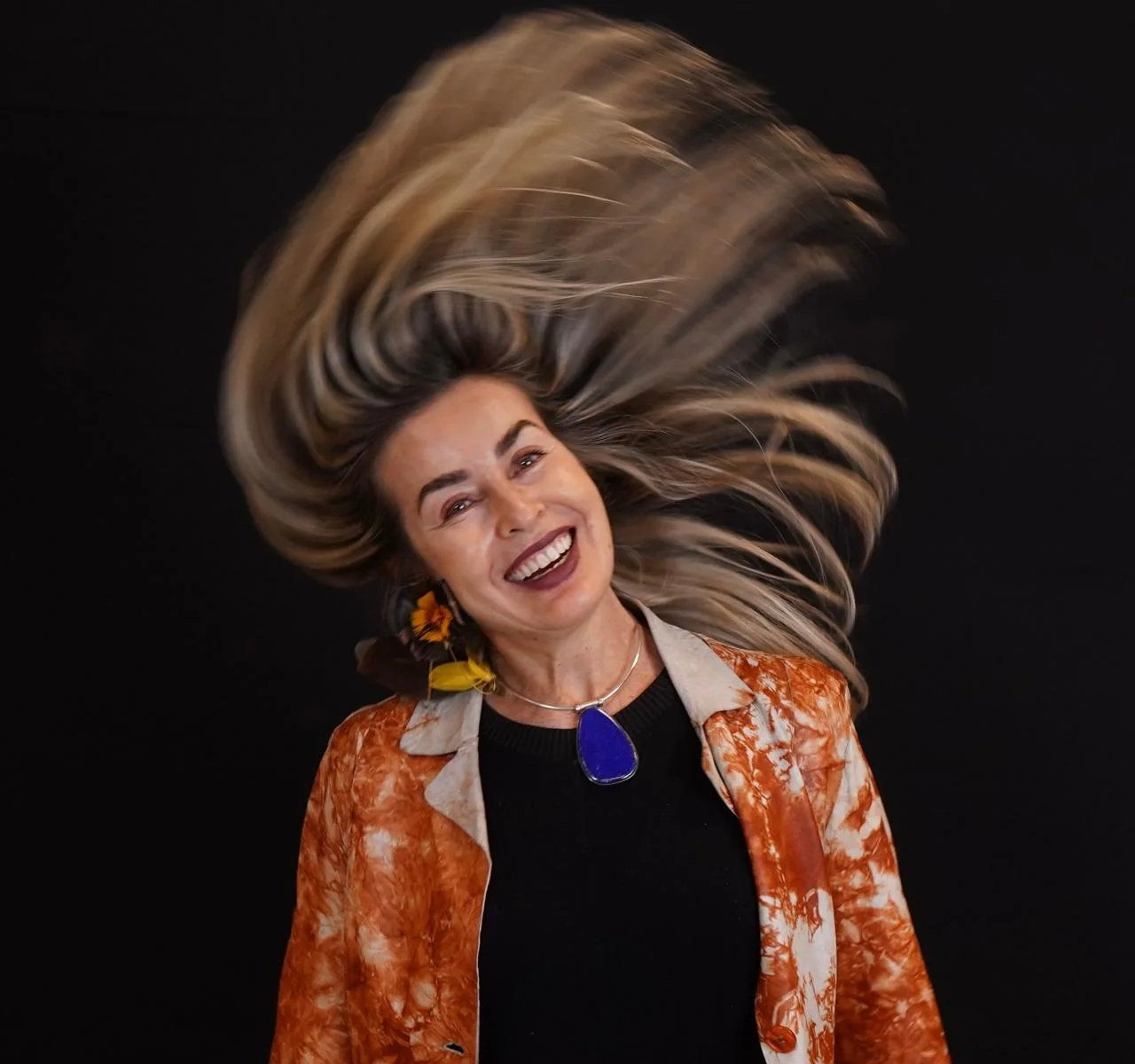 Daniella Prestes em movimento cênico, cabelo no ar, blazer laranja
